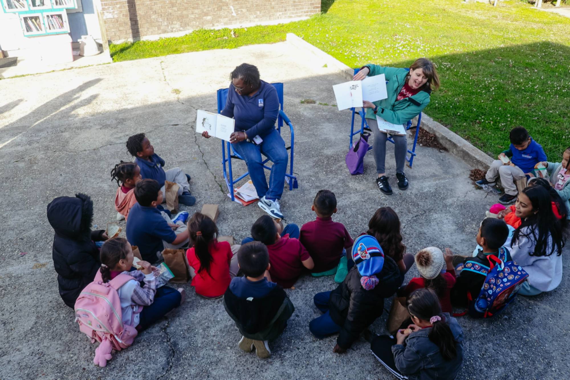 Outdoor bilingual story time circle with LSU educators and children gathered around open books.