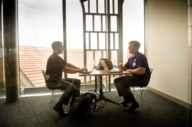 Two male students study at table with laptops