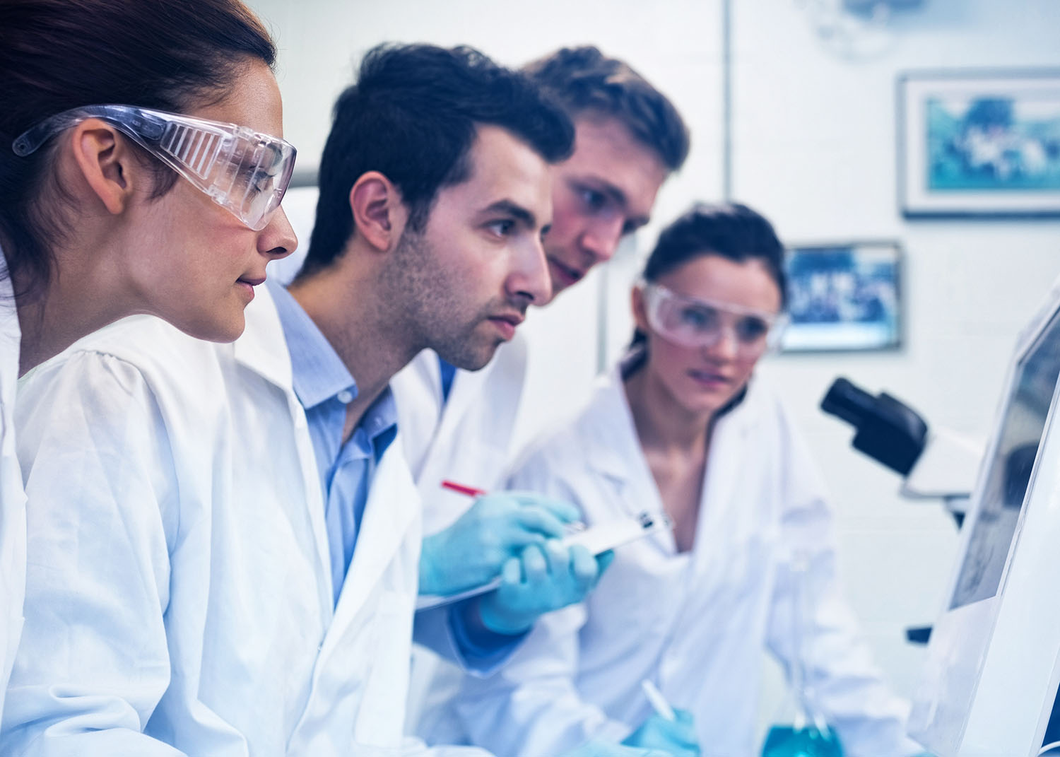 researchers in white lab coats looking at a computer screen