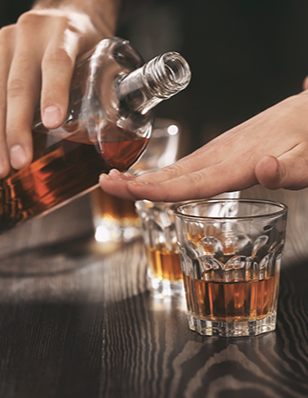 Photo of a hand over a glass stopping another person from pouring additional alcohol in the glass.